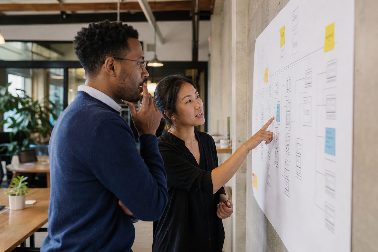 Two colleagues reviewing a printed website sitemap in a coworking space