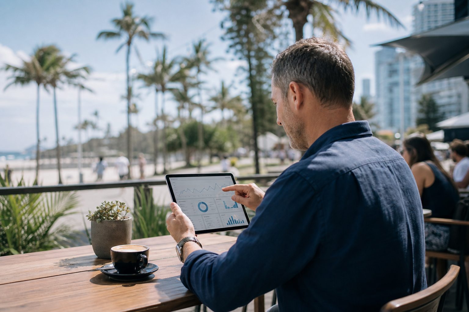 Business owner reviewing website AI visibility analytics on a tablet at a Gold Coast beachfront cafe