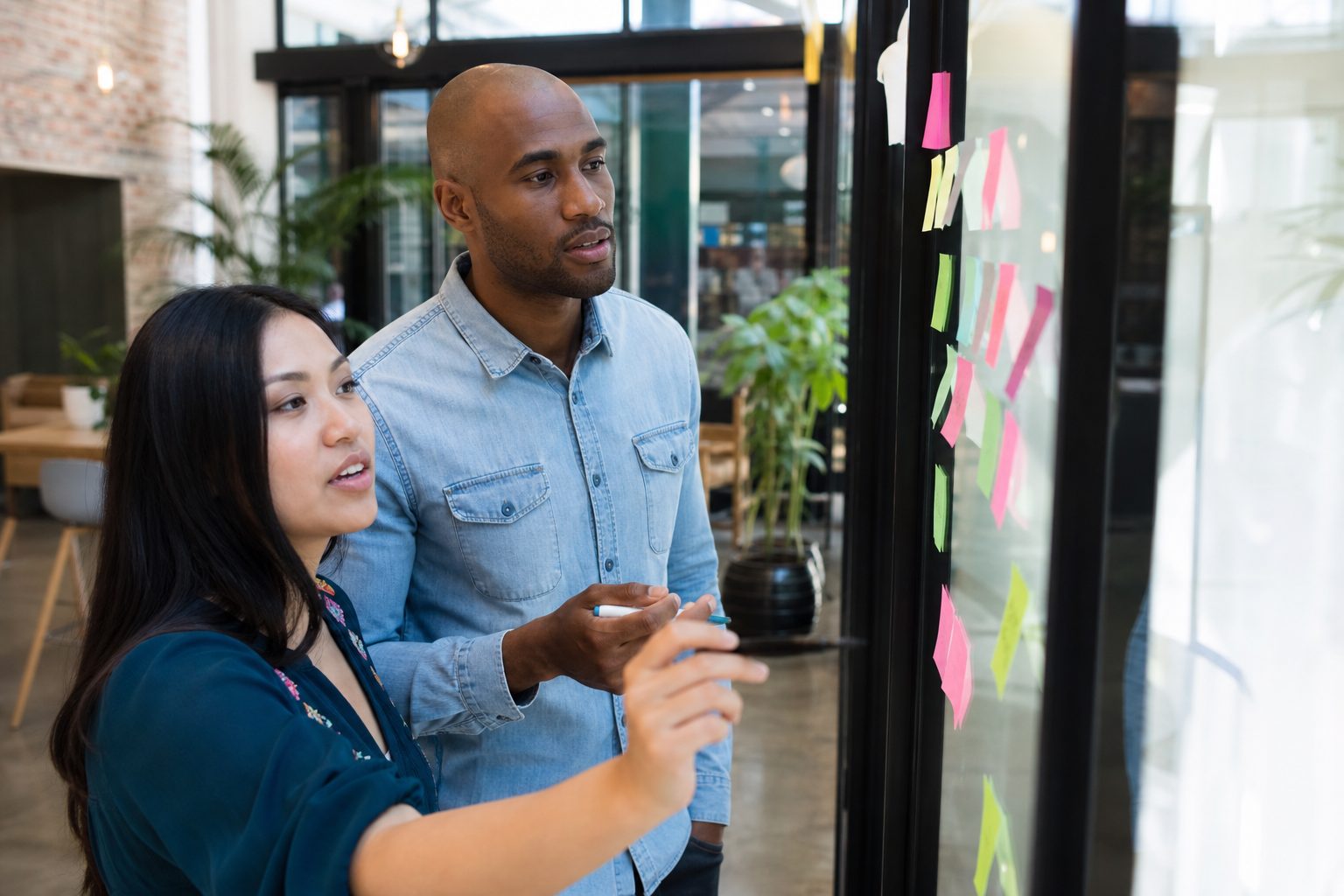 Developer and content strategist mapping page structure with sticky notes on a glass wall in a coworking space