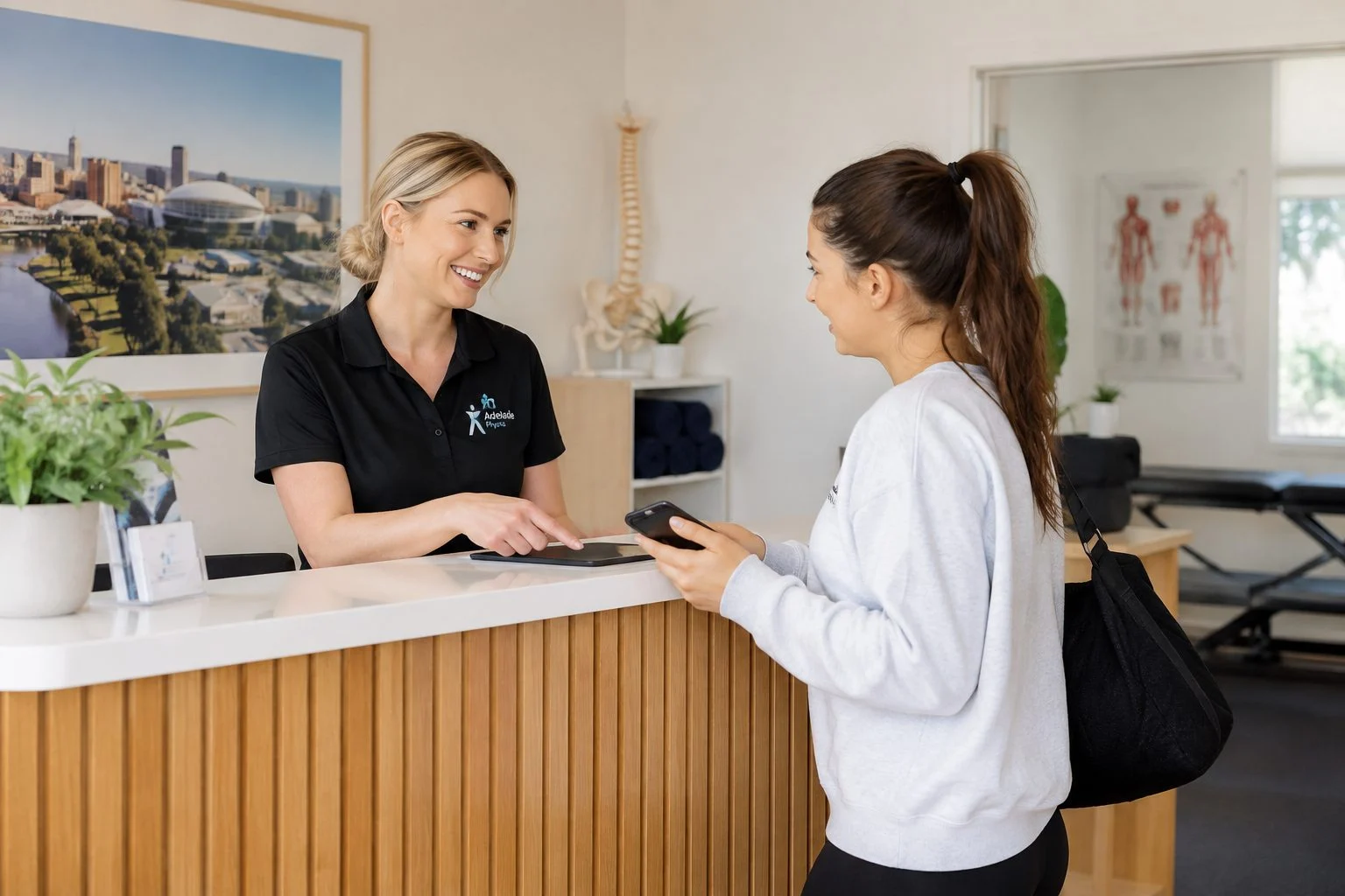 Adelaide physiotherapist speaking with a new patient holding a smartphone at the clinic front counter