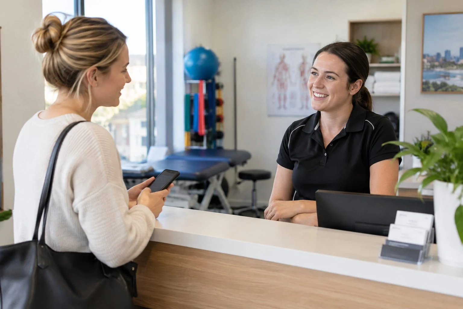 Adelaide physiotherapist speaking with a new patient holding a smartphone at the clinic front counter